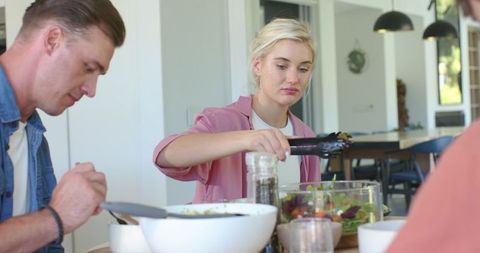 Woman serving fresh salad at casual family meal in open-plan kitchen