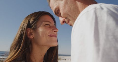 Happy caucasian couple embracing and looking at each other at beach on sunny day. Vacation, summer nature and lifestyle, unaltered.