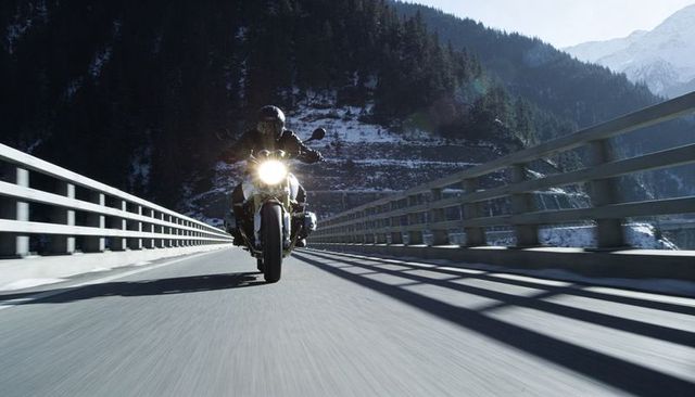 Riding sport motorcycle across snowy alpine bridge at high speed with glaring headlight