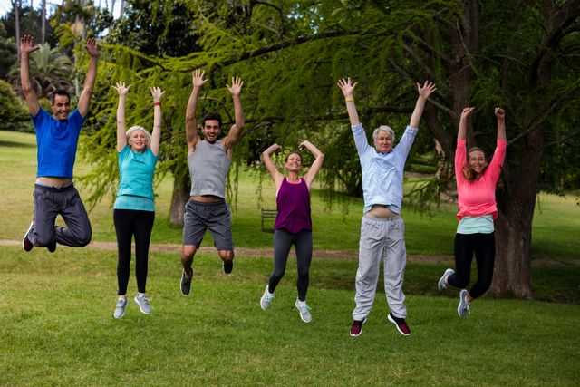 Group of diverse people jumping together in a park during an exercise session. Ideal for promoting fitness, healthy lifestyle, outdoor activities, teamwork, and community events. Perfect for use in health and wellness campaigns, fitness blogs, and outdoor activity promotions.