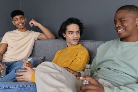 Multiracial friends relaxing on sofa sharing snacks and drinks during casual home hangout