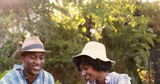 A young African American couple enjoys a sunny day outdoors, wearing casual summer hats and smiling, with copy space. Their cheerful expressions and relaxed attire suggest a moment of leisure and happiness.