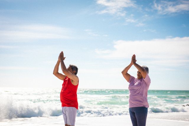 Senior man and woman in sportswear practicing tree pose yoga on a sunny beach. Ideal for promoting active lifestyles, wellness programs, retirement activities, and outdoor fitness routines.