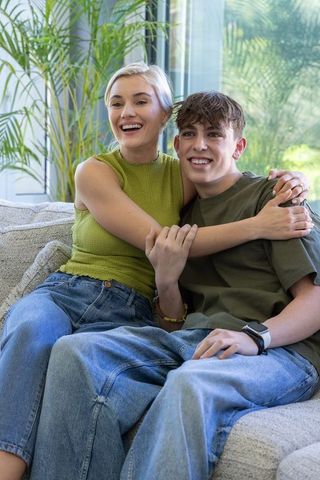 Smiling mother hugging teenage son on sofa in sunlit living room showing warm family bond