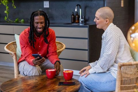 Friends laughing and chatting over coffee in modern kitchenette lounge with red mugs