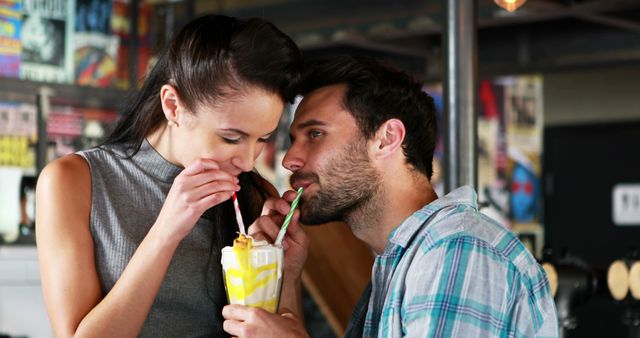 Young couple sharing a milkshake in a modern cafe. Enjoying a romantic moment while drinking from straws. Perfect for themes of love, dating, romance, young lifestyle, and modern relationships.