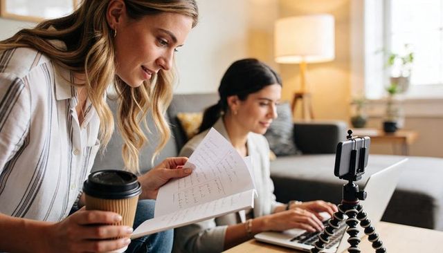 Remote content creators collaborating at home with laptop, notes and flexible phone tripod