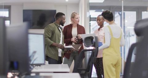 Reviewing documents together in open-plan office, diverse team collaborating around laptop
