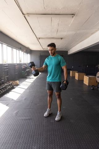Man lifting hex dumbbells on rubber gym floor for strength training and fitness workout