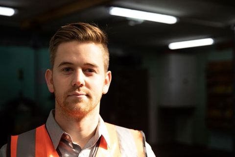Man wearing safety vest in workshop under fluorescent lighting