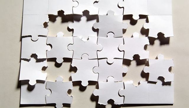 White Cardboard Jigsaw Puzzle with Torn Ragged Edges and Dramatic Shadows Showing Missing Pieces