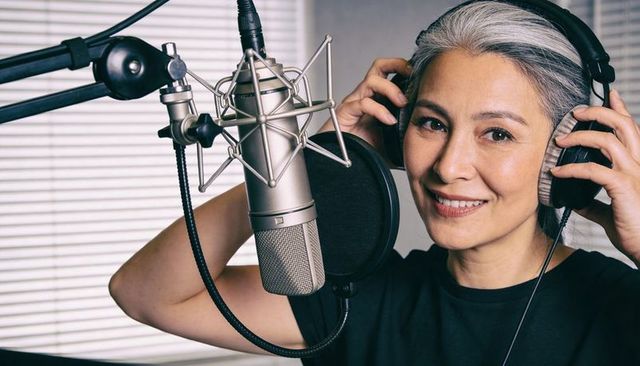 Senior asian voice talent recording podcast in studio with headphones and condenser mic