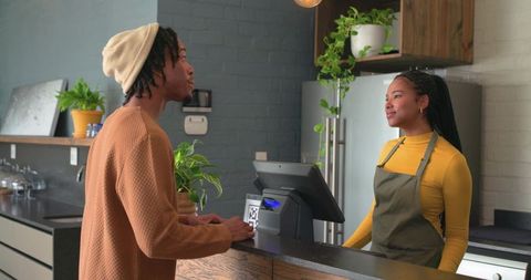 Barista greeting customer at counter in cozy green coffeehouse with rustic modern vibe