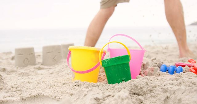 Colorful Sand Buckets on Beach with Person in Background - Download Free Stock Images Pikwizard.com