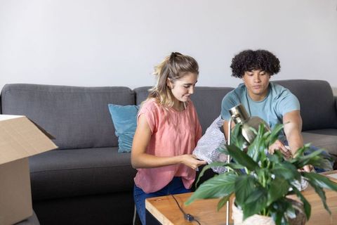 Young couple unpacking living room items, organizing lamp and plant on coffee table