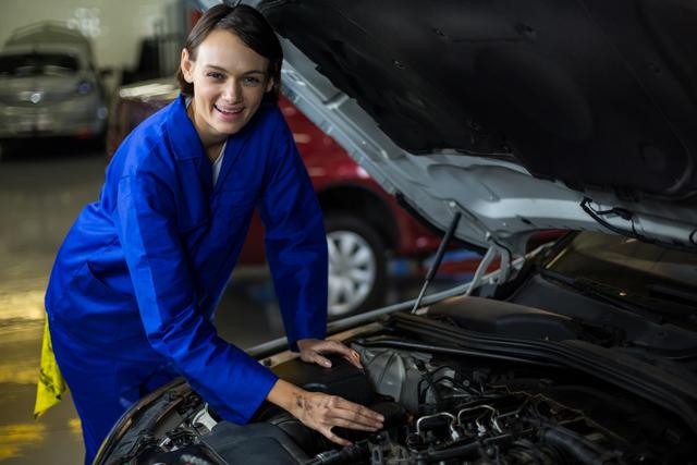 Female mechanic smiling while examining a car in repair garage