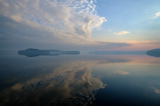 Lake at sunrise with calm water reflecting clouds in the sky. Perfect for promoting relaxation, meditation content, travel and tourism, nature blogs, and decor for soothing spaces. Captures tranquility and beauty of natural landscapes, making it ideal for wellness and mindfulness campaigns.