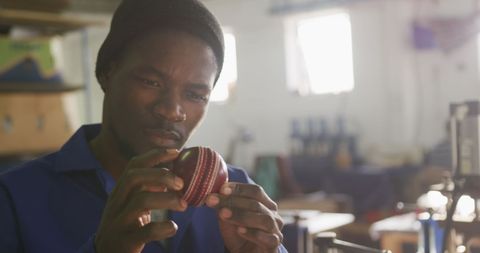 Man Carefully Inspecting Cricket Ball in Factory Workshop