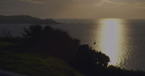 Golden Sun Path Crossing Calm Sea at Dusk with Silhouetted Headland, Tower and Lone Boat