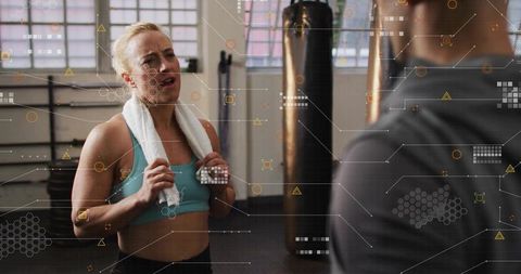 Female Athlete Catching Breath and Talking with Trainer by Punching Bag with HUD Overlay