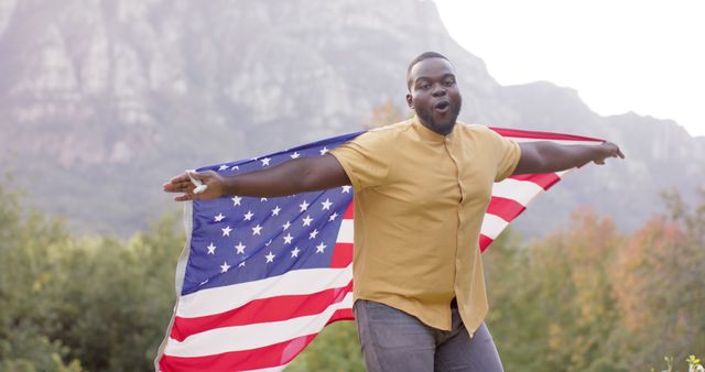 Person holding a USA flag with outstretched arms in an outdoor mountain region, showing excitement and joy. Suitable for themes of patriotism, freedom, celebration, and nature. Ideal for use in promotions for national holidays, patriotic events, or outdoor activities.