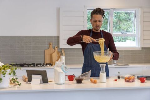 Man in denim apron mixing batter on kitchen island while following tablet recipe instruction