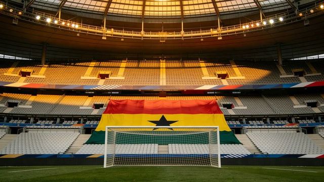 Ghana flag draped behind soccer goal in empty dome stadium with golden light