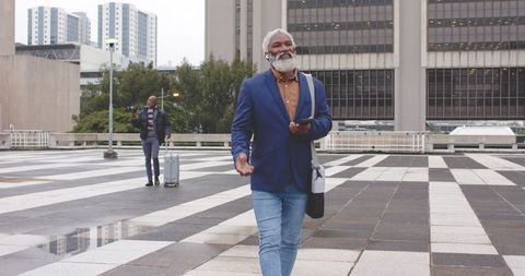 Mature african american professionals walking urban plaza pulling luggage using smartphone