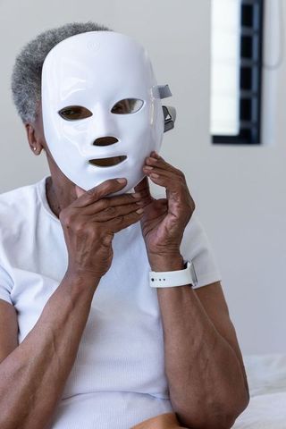 Senior african woman wearing led facial mask and smartwatch holding beautytech device