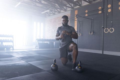African american athlete resting between kettlebell sets holding water bottle in sunlit gym
