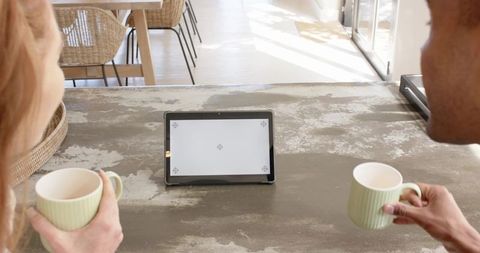 Couple sharing morning coffee while watching tablet on sunlit rustic dining table