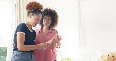 African American Couple Examining Pink Baby Outfit in Bright Nursery, Parenting Moment