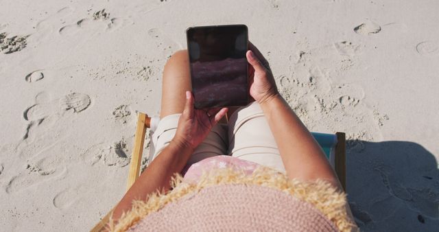 Biracial senior woman sitting on sunbed and using a smartphone at the beach. healthy outdoor leisure time by the sea.