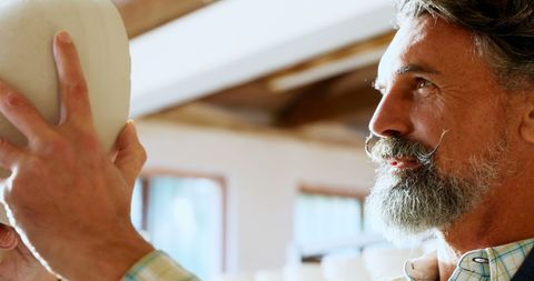 Senior man inspecting clay pot in art studio with intensity