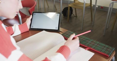 Student Writing Notes on Tablet and Notebook in Classroom