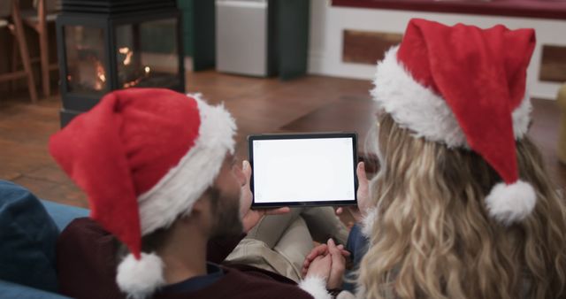 Couple with Santa hats using tablet in cozy living room - Download Free Stock Images Pikwizard.com