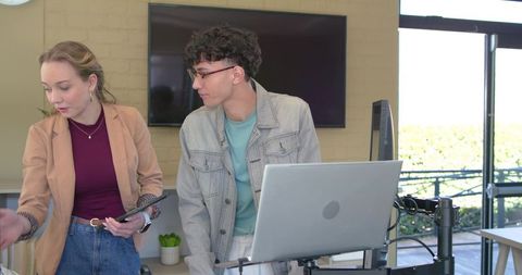 Young professionals collaborating on laptop presentation at lectern in modern office