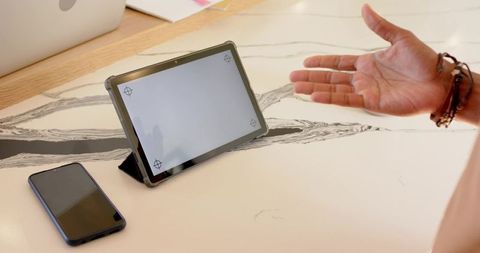 Tablet on folio stand on marble countertop with hand presenting smartphone and bracelets