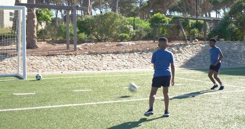 African american teen boys practicing soccer on turf near goal kicking ball during training