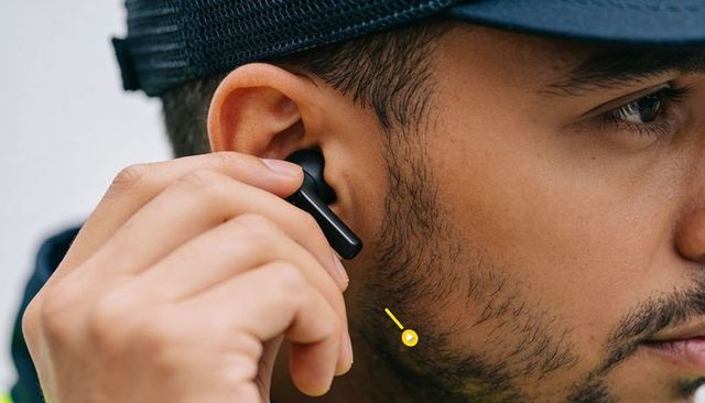 Young man adjusting wireless earbud wearing mesh cap close-up side profile bluetooth urban