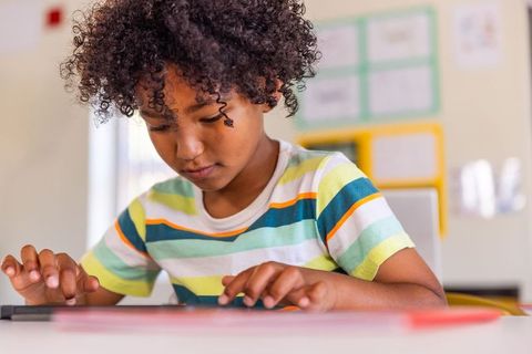 School-age child using tablet for focused classroom learning in colorful striped tee