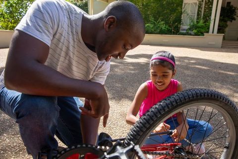 Father and daughter repair bike together in sunny driveway
