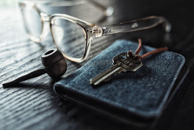Collection of everyday essentials including glasses, a pipe, a key, and a wallet on a wooden table. Can be used for lifestyle blogs, minimalist living articles, or daily essentials themes. Illustrates simple, casual, and essential items.