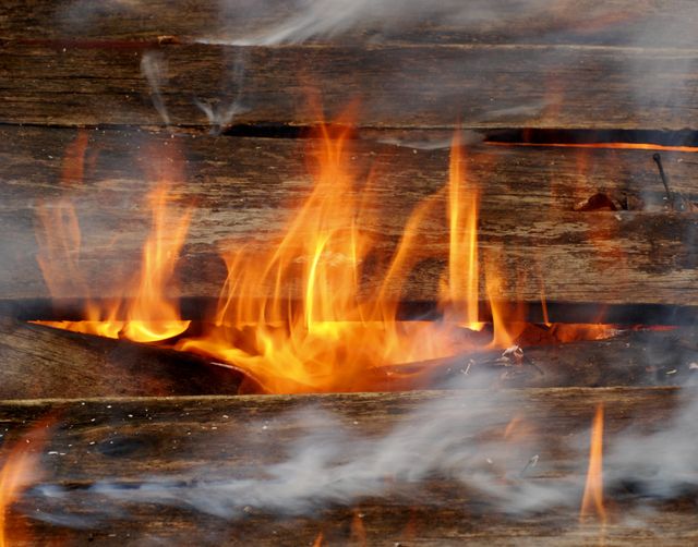 Wood is burning with visible flames and smoke. This is ideal for articles about fire safety, survival techniques, or natural disasters. Can be used in materials related to campfires, emergency response, and fire prevention.