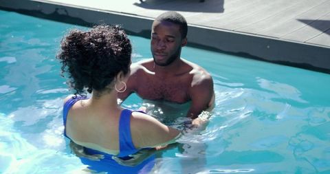 Indian woman and african american man chatting waist-deep in sunlit pool