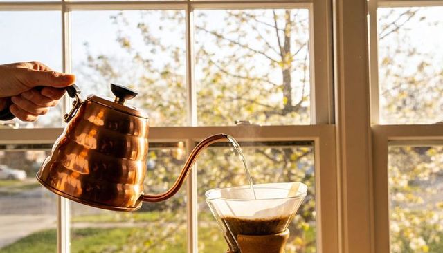 Copper gooseneck kettle pouring over chemex dripper at sunlit autumn window
