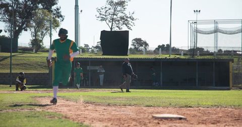 Baseball player sprinting from home plate in green uniform at community ballpark