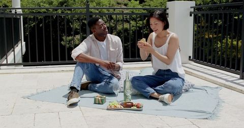 Diverse couple enjoying urban rooftop picnic with fresh snacks