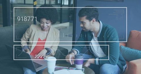 Young Professionals Collaborating Over Laptop with Digital Data Overlay in Office Lounge