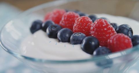 Creamy yogurt topping fresh blueberries and raspberries in glass dessert bowl